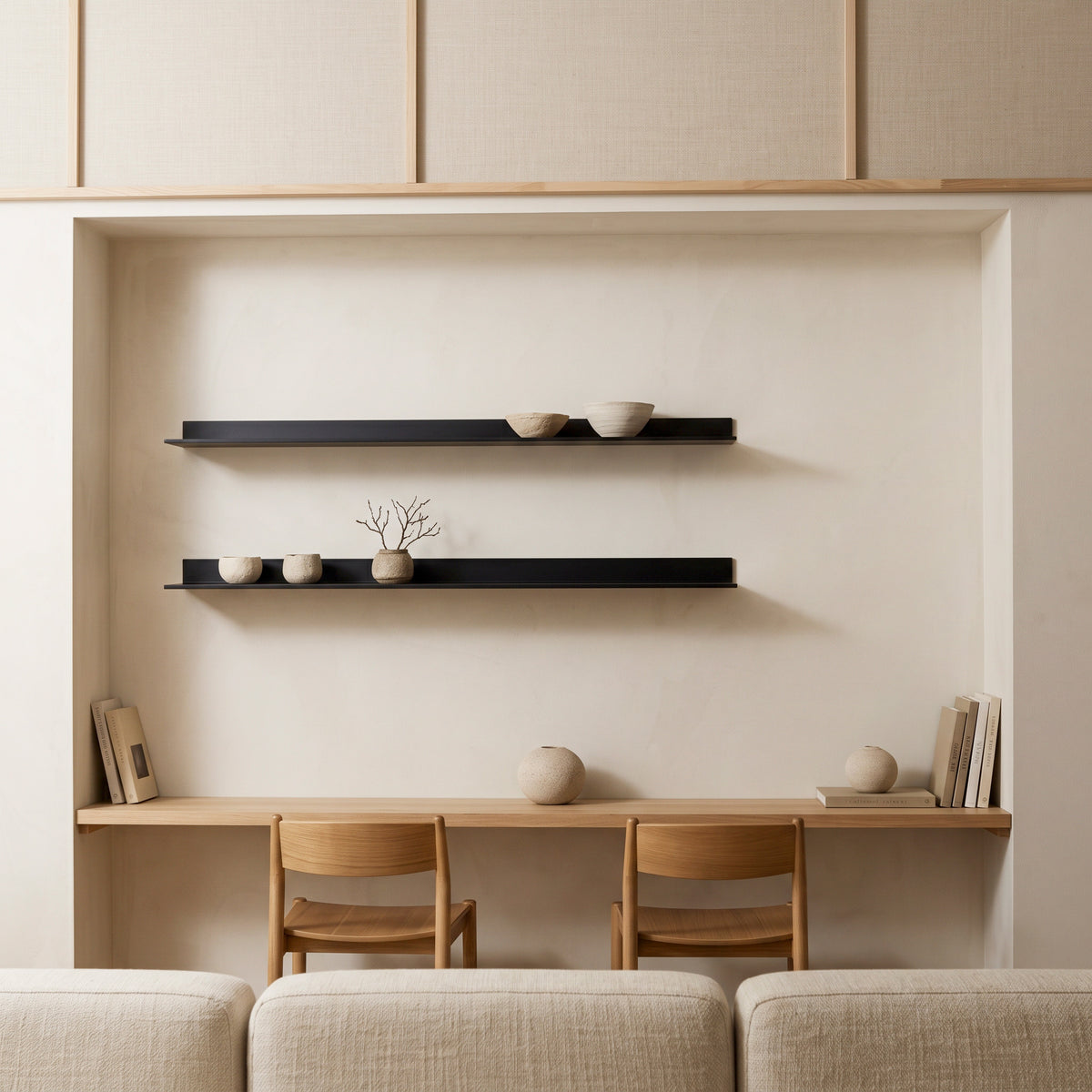Two black aluminum floating display shelves installed inside a recessed wall niche, holding ceramic bowls and branches